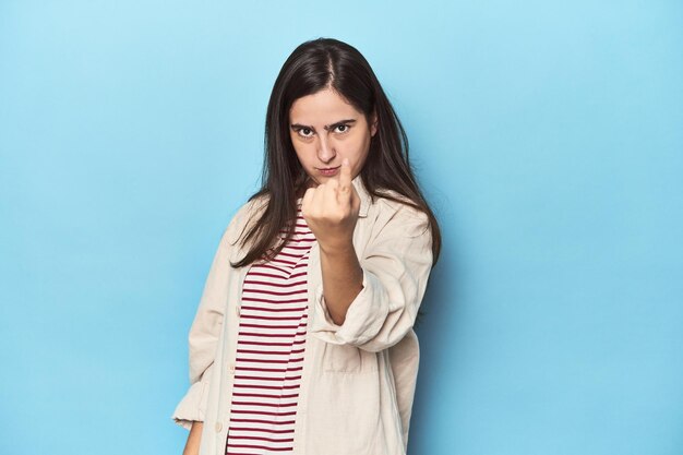 Young Caucasian woman on blue backdrop pointing with finger at you as if inviting come closer