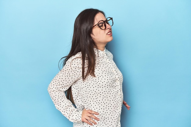 Young Caucasian woman on blue backdrop suffering a back pain