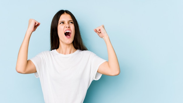 Young caucasian woman on blue wall raising fist after a victory