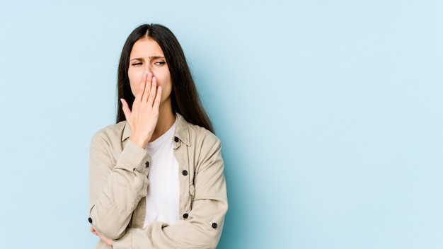 Young caucasian woman on blue wall yawning showing a tired gesture covering mouth with hand.