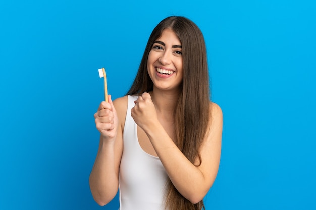 Young caucasian woman brushing teeth isolated on blue background celebrating a victory