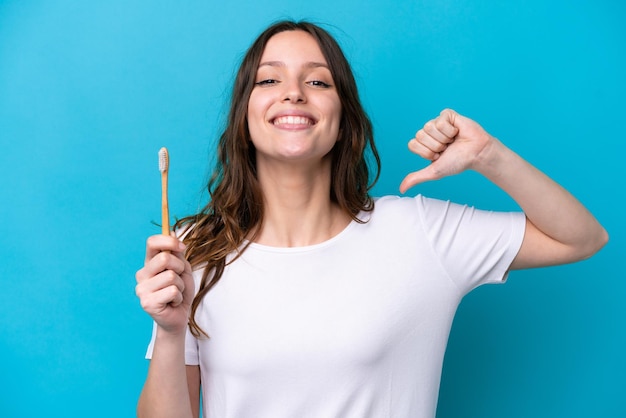 Young caucasian woman brushing teeth isolated on blue background proud and selfsatisfied