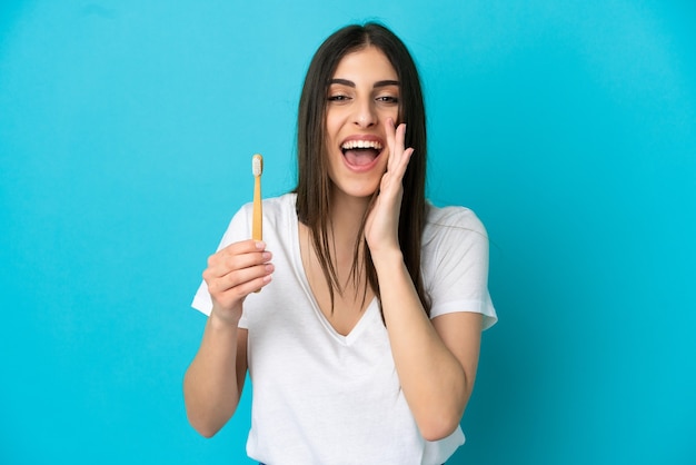 Young caucasian woman brushing teeth isolated on blue background shouting with mouth wide open