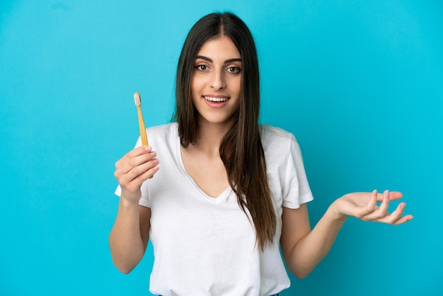 Young caucasian woman brushing teeth isolated on blue background with shocked facial expression