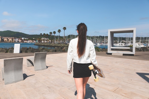 Young caucasian woman carrying a longboard at the sea side