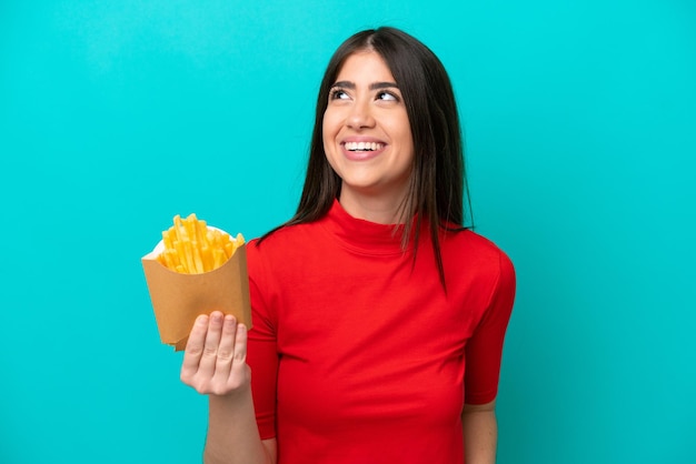 Young caucasian woman catching french fries isolated on blue background thinking an idea while looking up