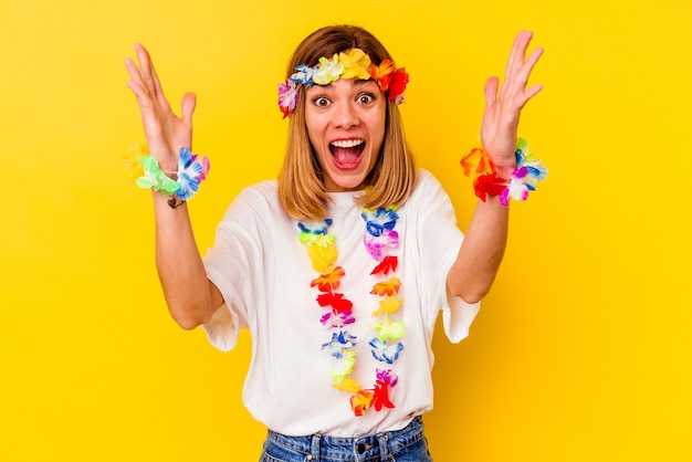 Young caucasian woman celebrating a hawaiian party isolated on yellow background receiving a pleasant surprise, excited and raising hands.