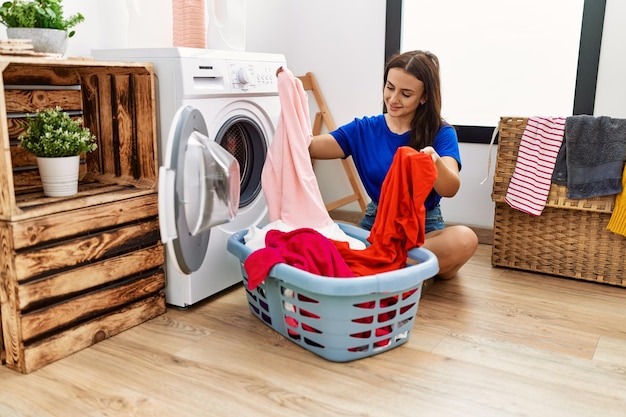 Young caucasian woman cleaning clothes using washing machine at laundry room