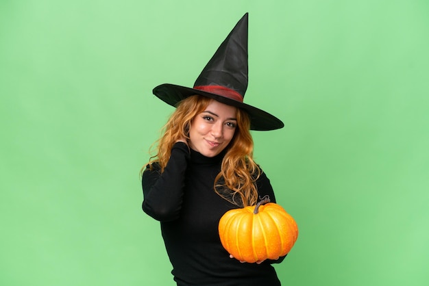 Young caucasian woman costume as witch holding a pumpkin isolated on green screen chroma key background laughing