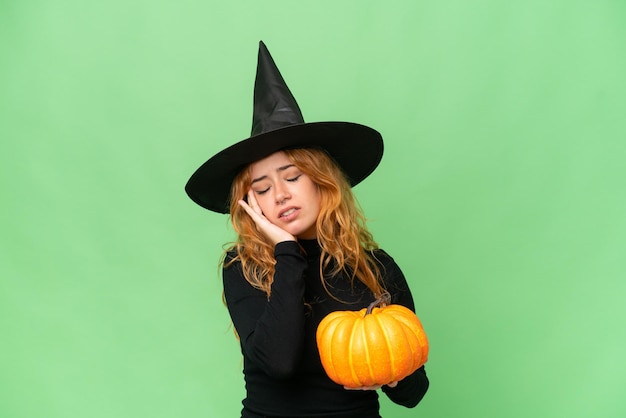 Young caucasian woman costume as witch holding a pumpkin isolated on green screen chroma key background with headache