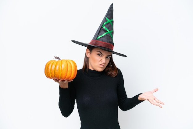 Young caucasian woman costume as witch holding a pumpkin isolated on white background making doubts gesture while lifting the shoulders