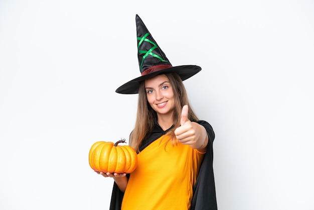 Young caucasian woman costume as witch holding a pumpkin isolated on white background with thumbs up because something good has happened