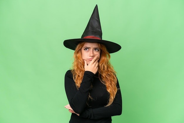 Young caucasian woman costume as witch isolated on green screen chroma key background having doubts and with confuse face expression