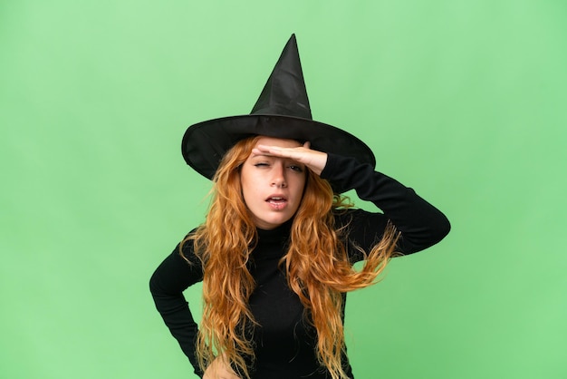 Young caucasian woman costume as witch isolated on green screen chroma key background looking far away with hand to look something