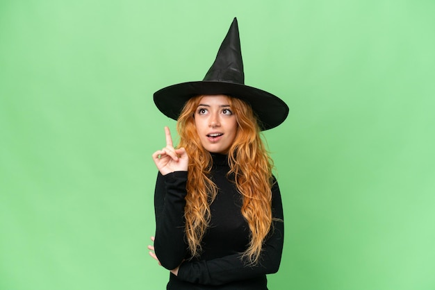 Young caucasian woman costume as witch isolated on green screen chroma key background thinking an idea pointing the finger up