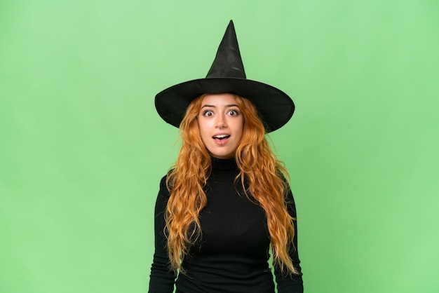 Young caucasian woman costume as witch isolated on green screen chroma key background with surprise facial expression