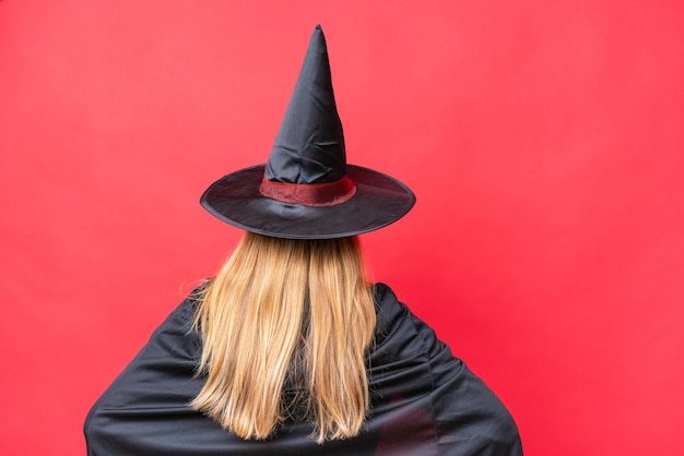 Young caucasian woman costume as witch isolated on red background in back position