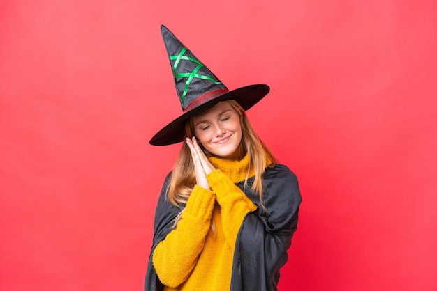 Young caucasian woman costume as witch isolated on red background making sleep gesture in dorable expression