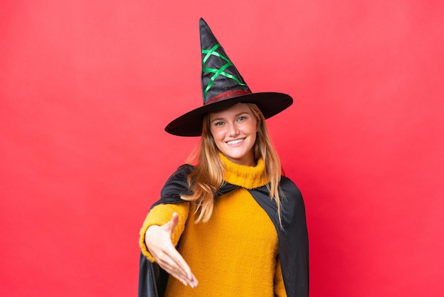 Young caucasian woman costume as witch isolated on red background shaking hands for closing a good deal