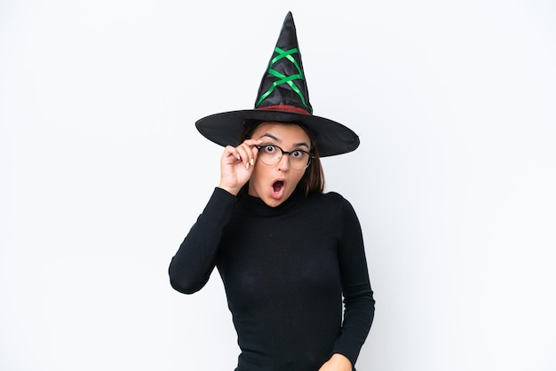 Young caucasian woman costume as witch isolated on white background with glasses and surprised