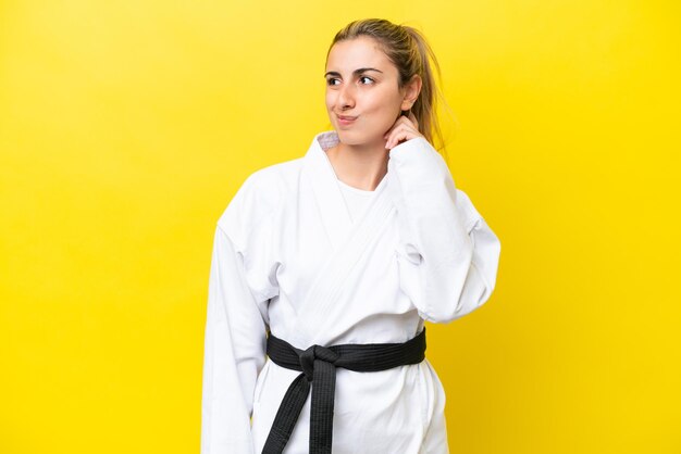 Young caucasian woman doing karate isolated on yellow background having doubts