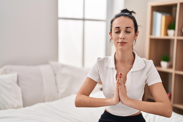 Young caucasian woman doing yoga exercise sitting on bed at bedroom