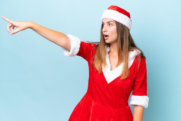 Young caucasian woman dressed as mama noel isolated on blue background pointing away