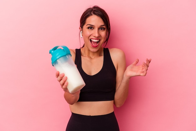 Young caucasian woman drinking a protein shake isolated on pink background