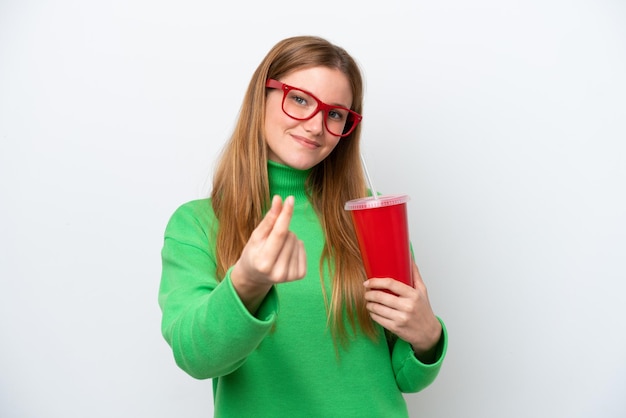 Young caucasian woman drinking soda isolated on white background making money gesture