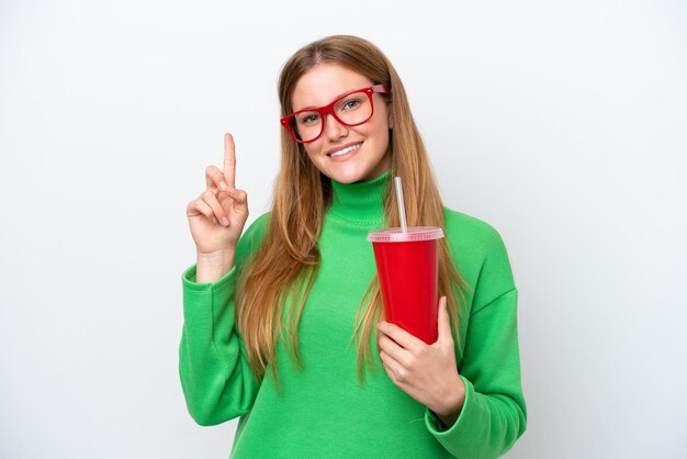 Young caucasian woman drinking soda isolated on white background showing and lifting a finger in sign of the best