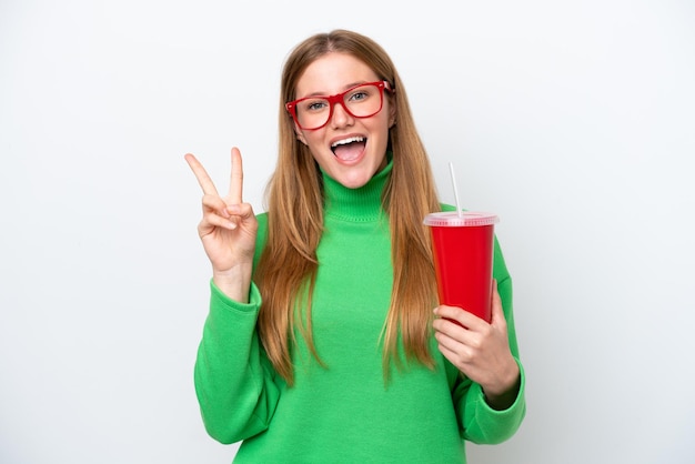 Young caucasian woman drinking soda isolated on white background smiling and showing victory sign