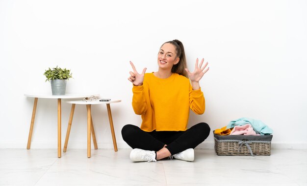 Young caucasian woman folding clothes sitting on the floor isolated on white background counting seven with fingers