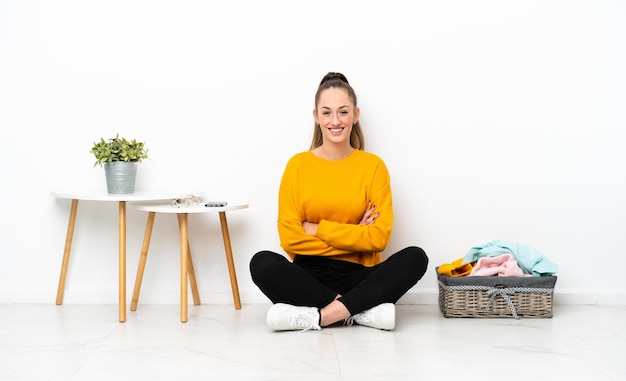 Young caucasian woman folding clothes sitting on the floor isolated on white background keeping the arms crossed in frontal position