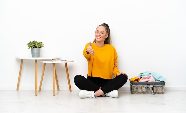 Young caucasian woman folding clothes sitting on the floor isolated on white background shaking hands for closing a good deal