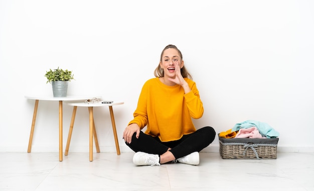 Young caucasian woman folding clothes sitting on the floor isolated on white background shouting with mouth wide open