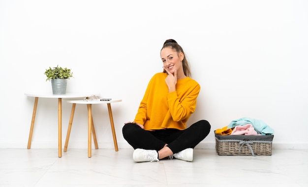 Young caucasian woman folding clothes sitting on the floor isolated on white background smiling