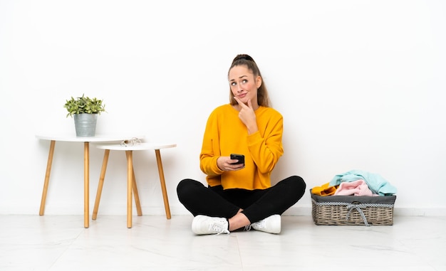 Young caucasian woman folding clothes sitting on the floor isolated on white background thinking and sending a message