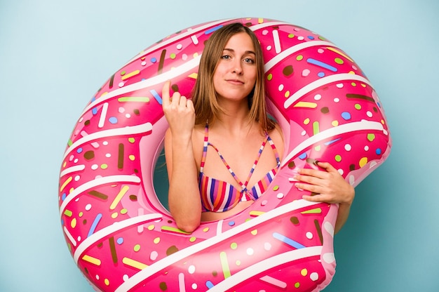 Young caucasian woman holding air mattress isolated on blue background pointing with finger at you as if inviting come closer