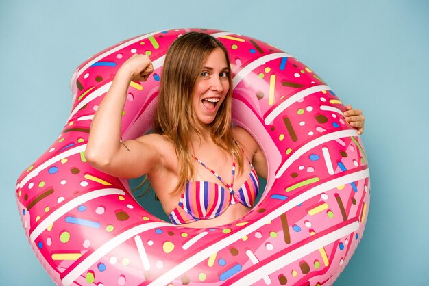 Young caucasian woman holding air mattress isolated on blue background