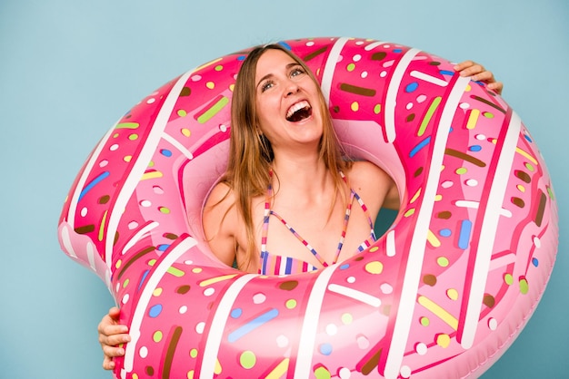 Young caucasian woman holding air mattress isolated on blue background