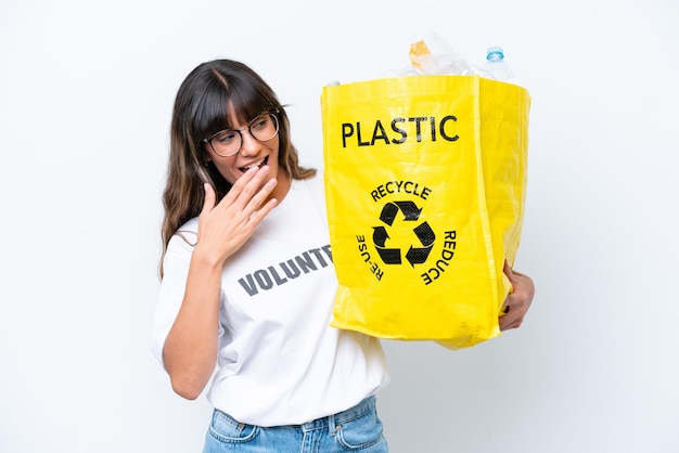 Young caucasian woman holding a bag full of plastic bottles to recycle isolated on white background with surprise and shocked facial expression