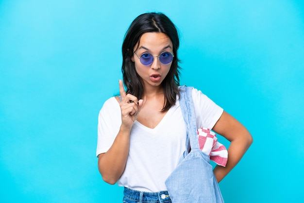 Young caucasian woman holding a beach bag isolated on blue background thinking an idea pointing the finger up