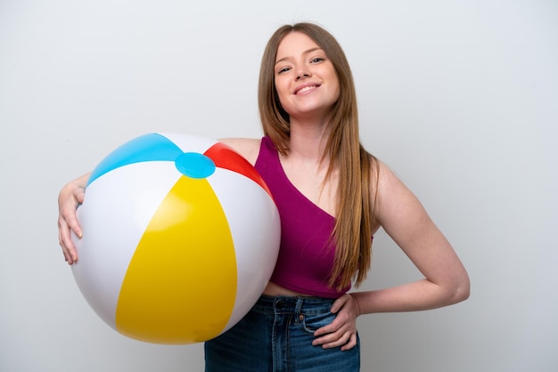 Young caucasian woman holding beach ball isolated on white background posing with arms at hip and smiling