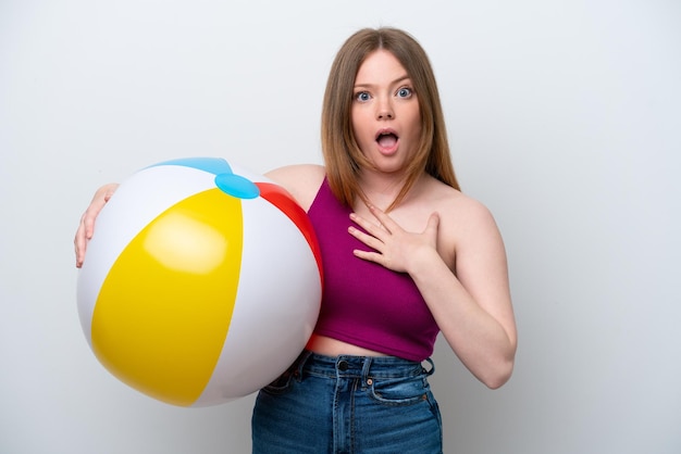 Young caucasian woman holding beach ball isolated on white background surprised and shocked while looking right