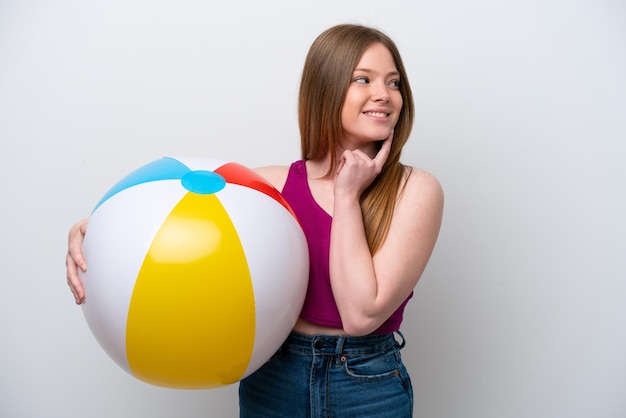 Young caucasian woman holding beach ball isolated on white background thinking an idea while looking up