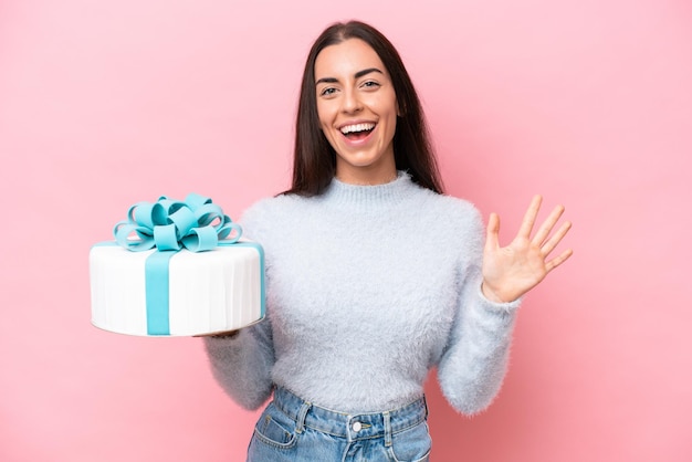 Young caucasian woman holding birthday cake isolated on pink background counting five with fingers