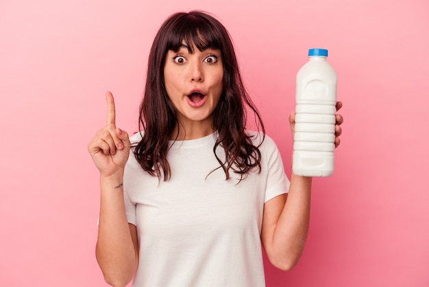 Young caucasian woman holding a bottle of milk isolated on pink wall having some great idea, concept of creativity.