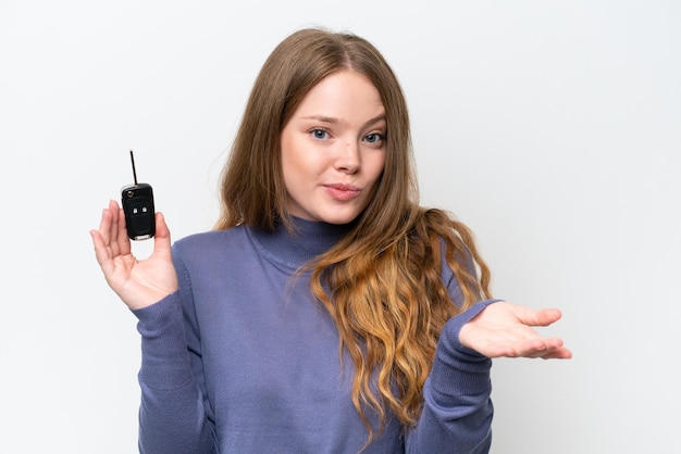 Young caucasian woman holding car keys isolated on white background making doubts gesture while lifting the shoulders