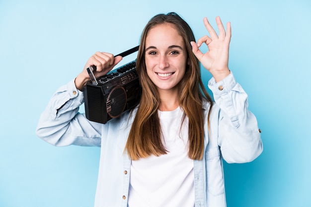 Young caucasian woman holding a cassete isolated cheerful and confident showing ok gesture.