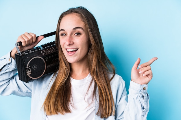 Young caucasian woman holding a cassete isolated smiling cheerfully pointing with forefinger away.